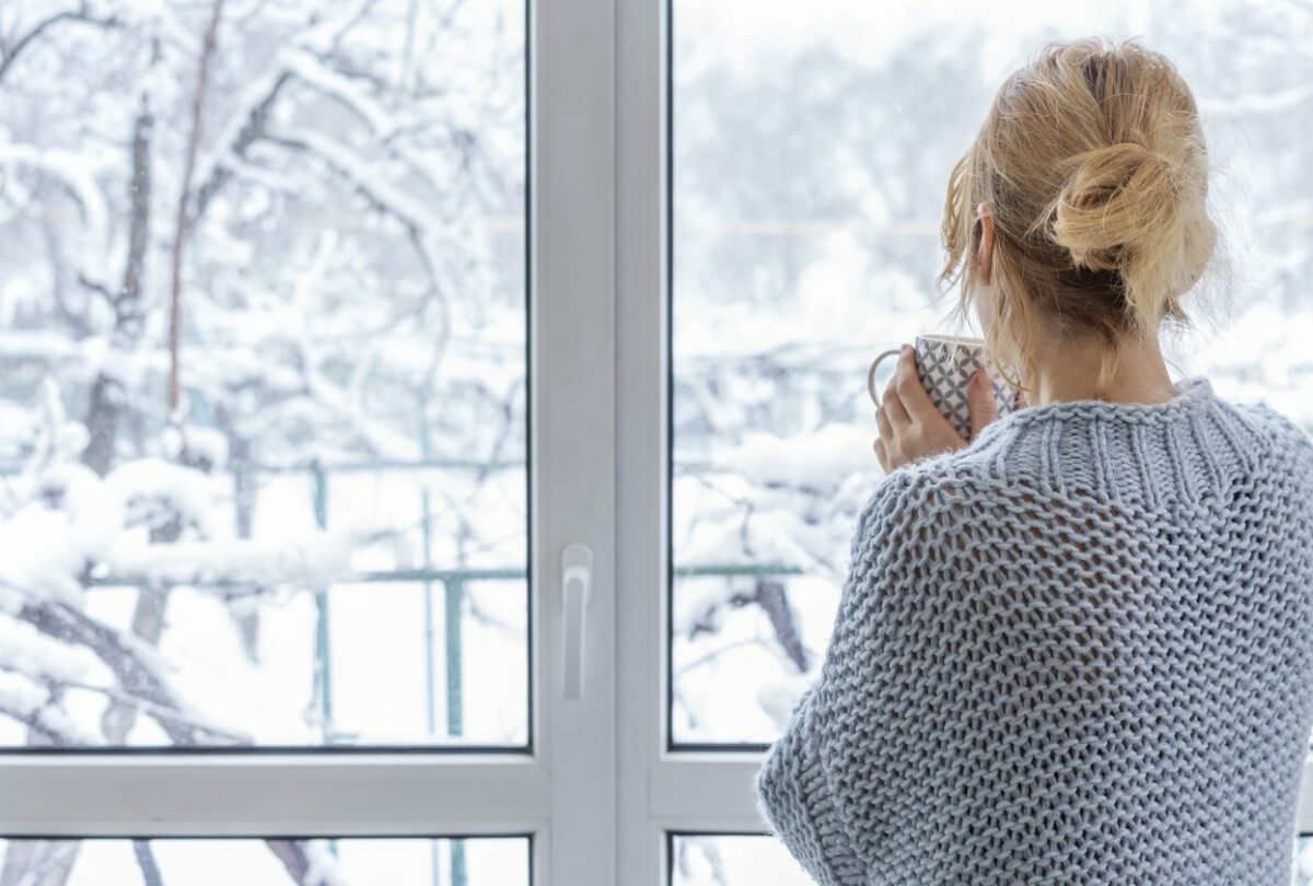 woman looking outside of the window to the snow