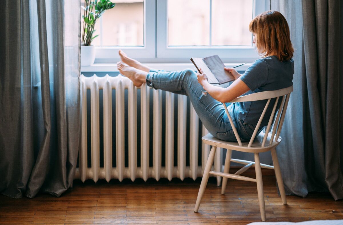 woman reading a book while having her feet on heater